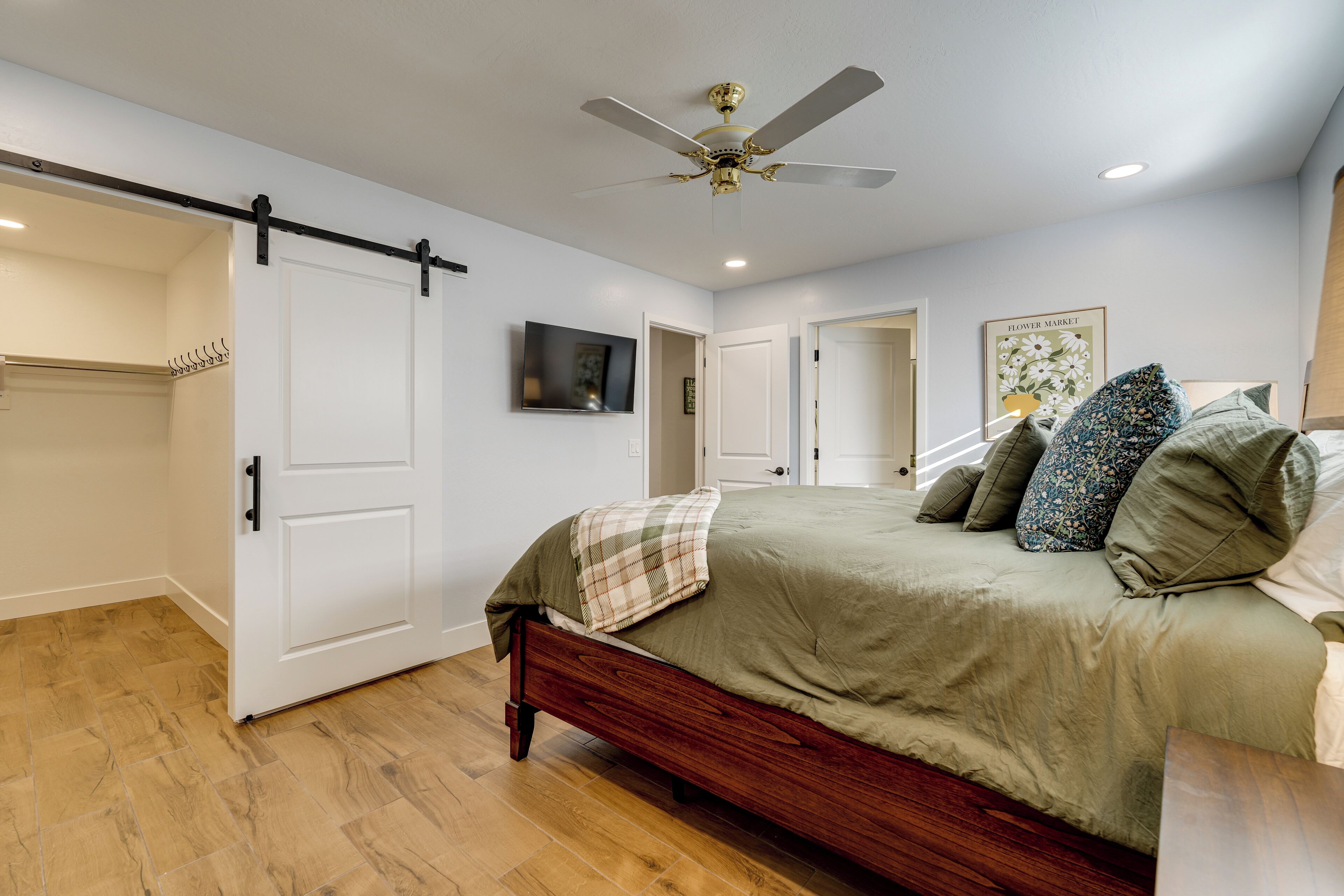 Un dormitorio con cama, ventilador de techo, televisor y puerta que da a otra habitación.