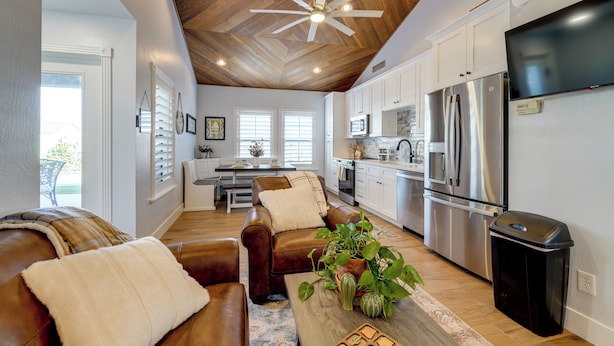 A spacious living room with a brown leather sofa and a wooden coffee table, a kitchen with white cabinets and stainless steel appliances, and a ceiling fan with wooden beams. - Private Pool & Hot Tub! Relaxing Mesa Apartment (Mesa)