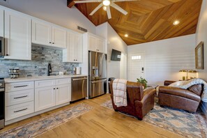 A spacious kitchen with white cabinets, a stone backsplash, and stainless steel appliances. There is a brown leather sofa and a small table with a lamp in the living area. - Private Pool & Hot Tub! Relaxing Mesa Apartment (Mesa)