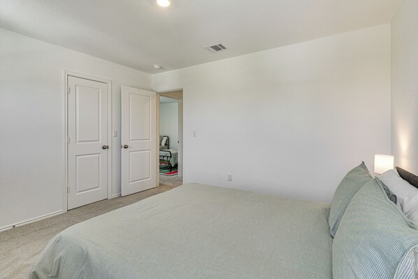 A bedroom with a large bed, two white doors, and a visible closet. - 6 Mi to Mckinney Falls: Spacious Home w/ Game Room (Austin)
