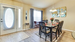 Een eetruimte met een tafel gedekt voor zes personen, omringd door stoelen, een vaas met bloemen en een kroonluchter.