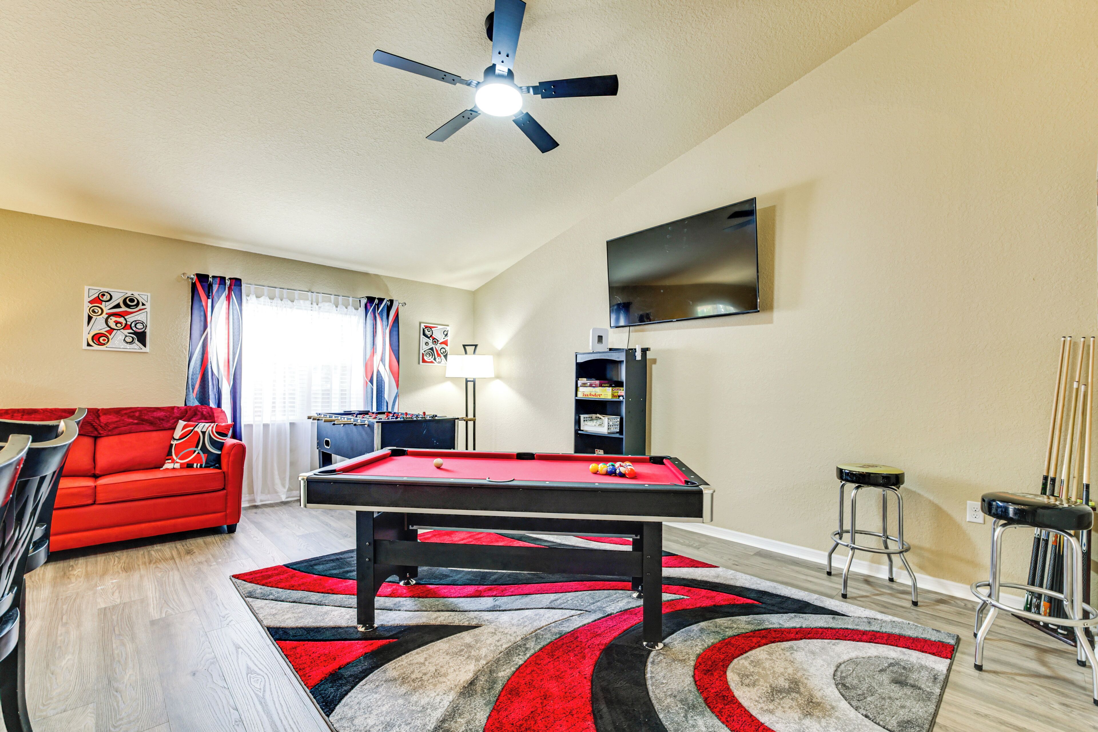 A living room with a pool table, a red sofa, a ceiling fan, and a flat-screen TV mounted on the wall.