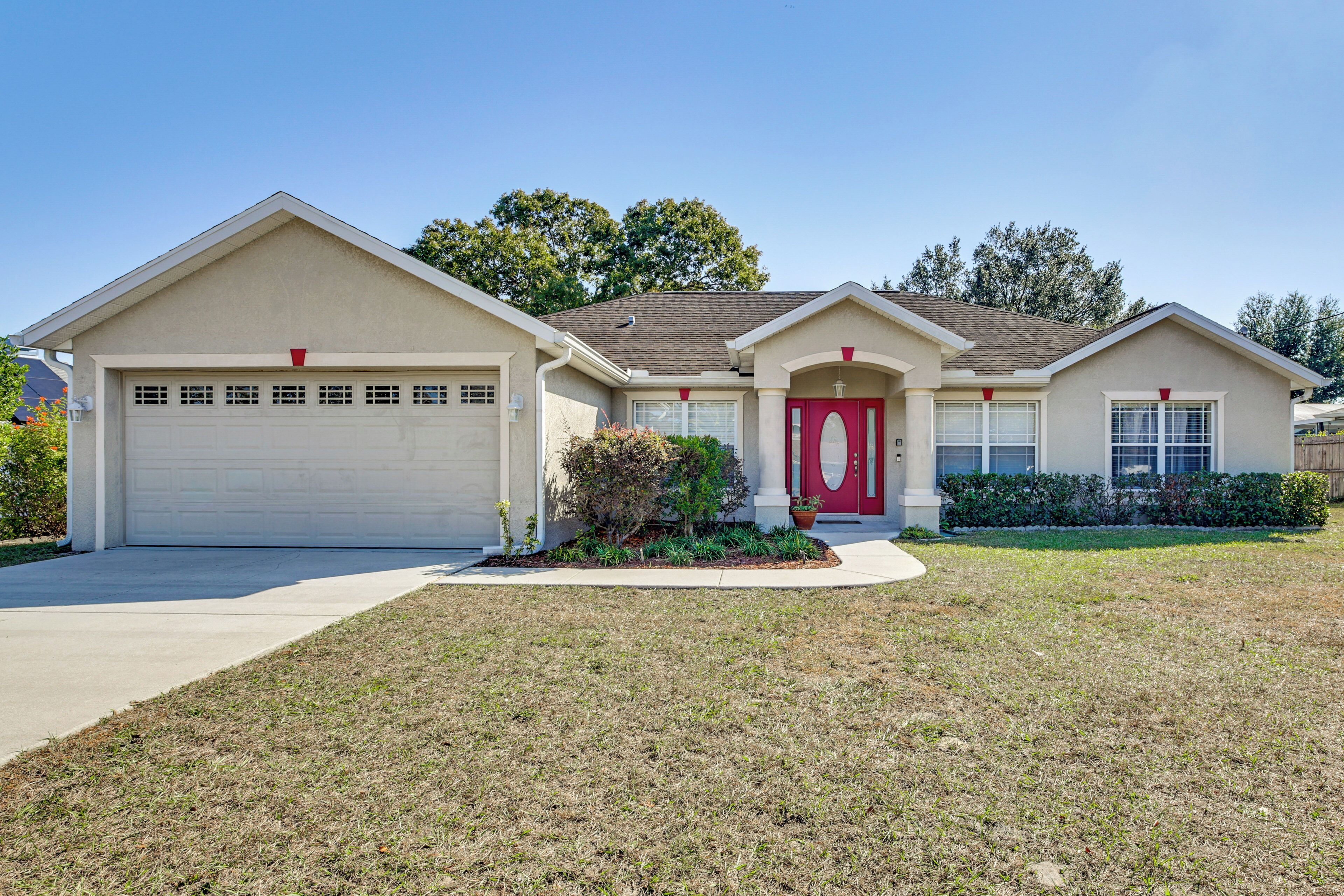 A single-story house with a garage, a red front door, and a small front yard with a potted plant.