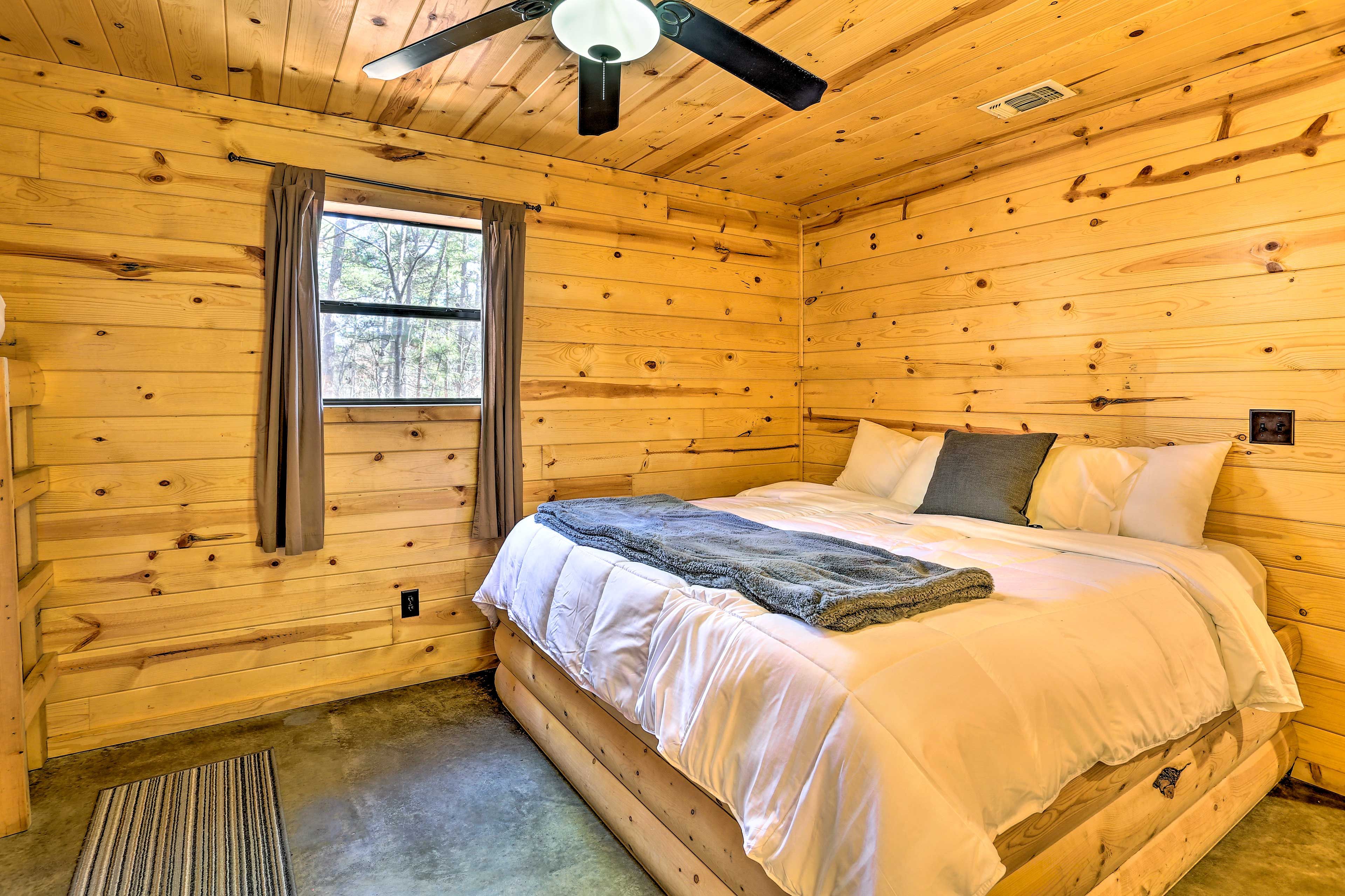 A wooden cabin bedroom with a bed, a ceiling fan, and a window.