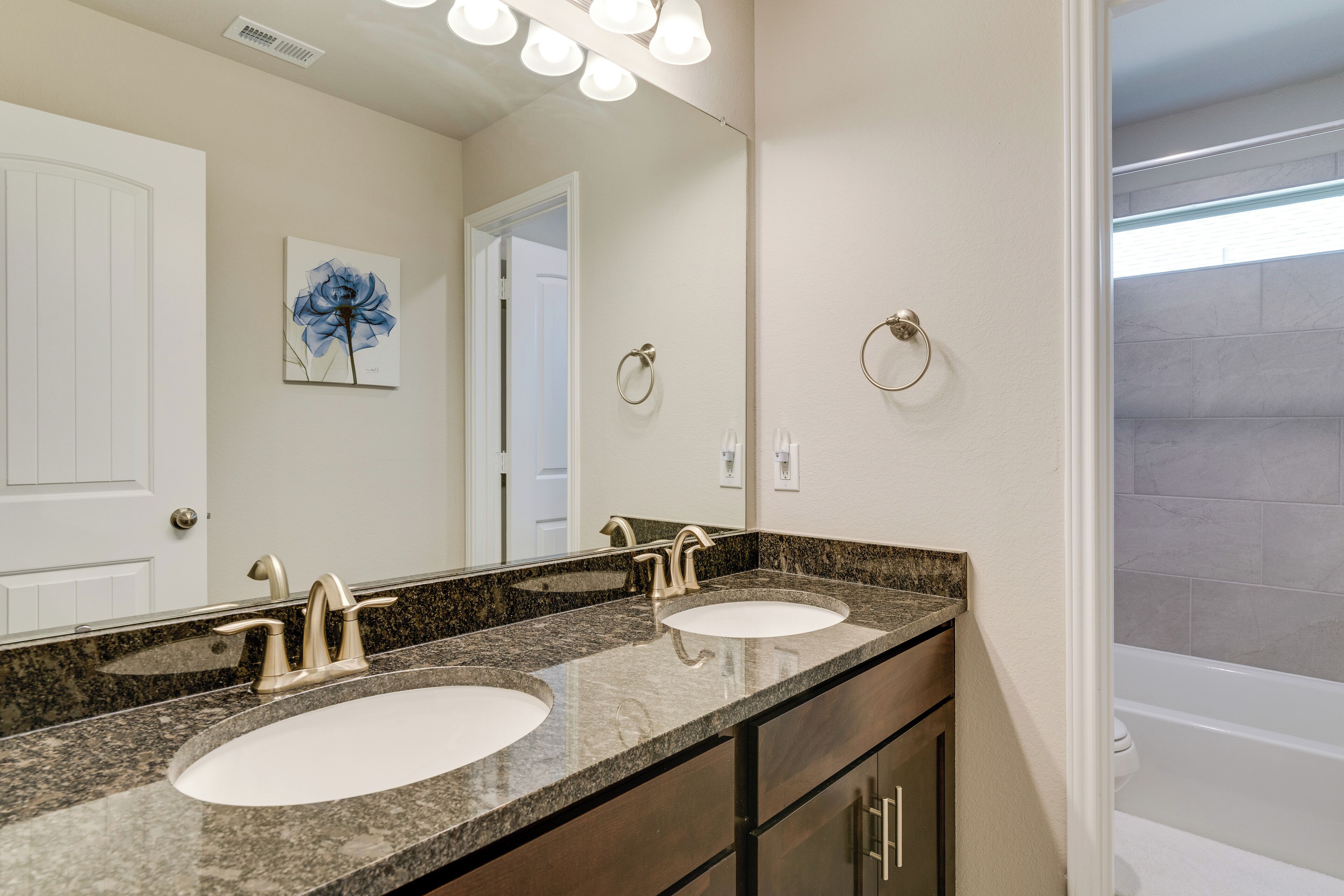 Un baño con dos lavamanos, un espejo grande y una puerta que da a otra habitación.