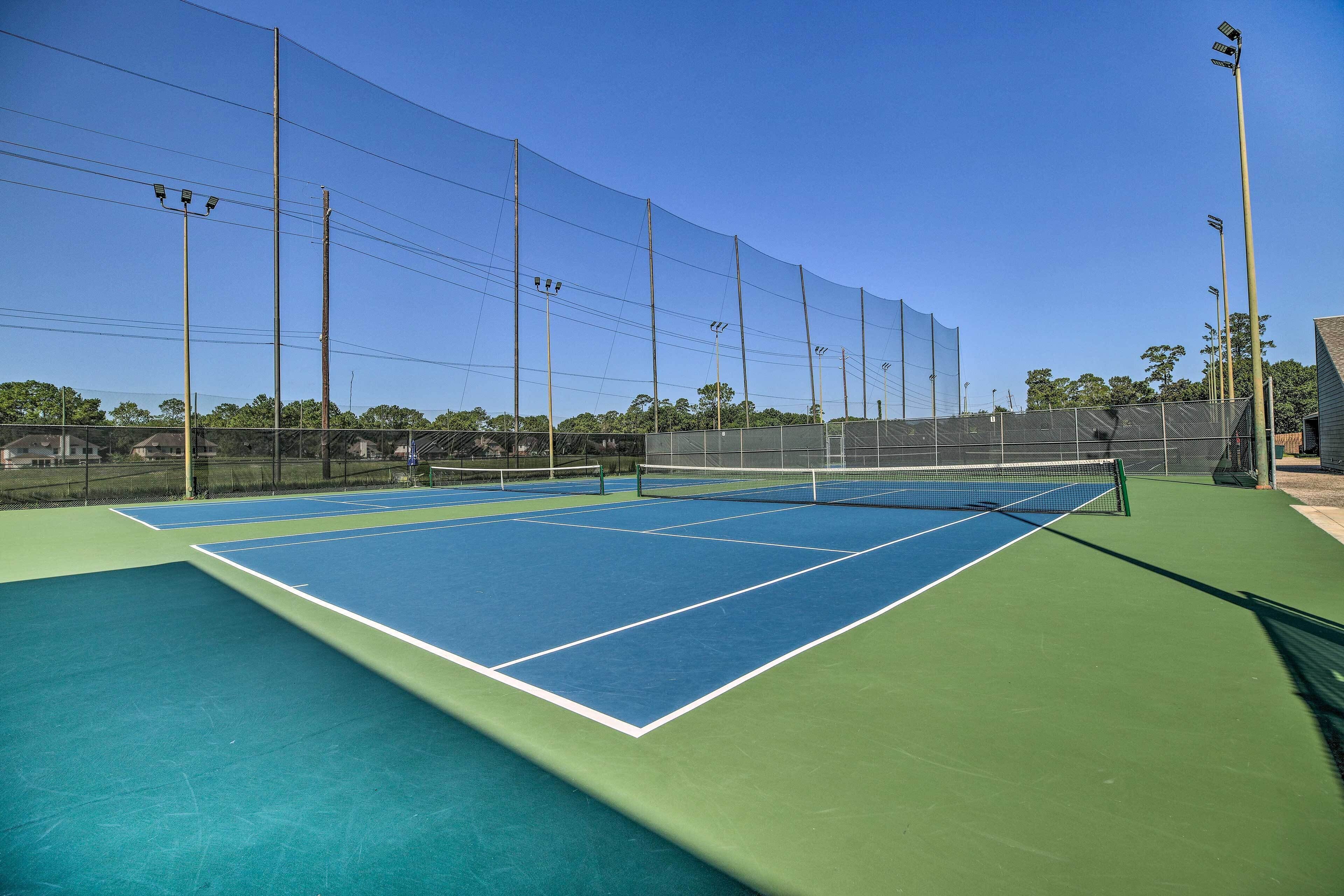 Una cancha de tenis con red, rodeada por una valla y postes de luz.