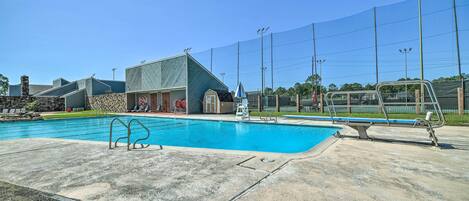 A swimming pool with a diving board, a lifeguard chair, and a fence.