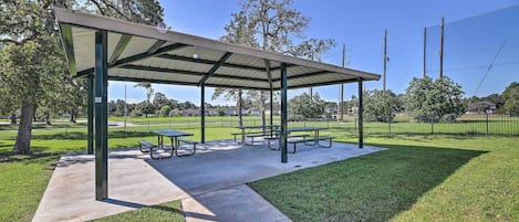 A covered picnic area with benches and picnic tables, surrounded by grass and trees.