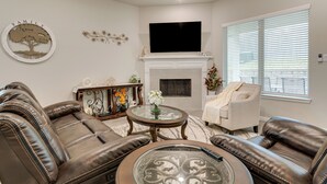 A living room with leather sofas, a glass coffee table, a fireplace, and a mounted TV. - Lake Conroe Home w/ Resort-style Perks & Patio (Montgomery)
