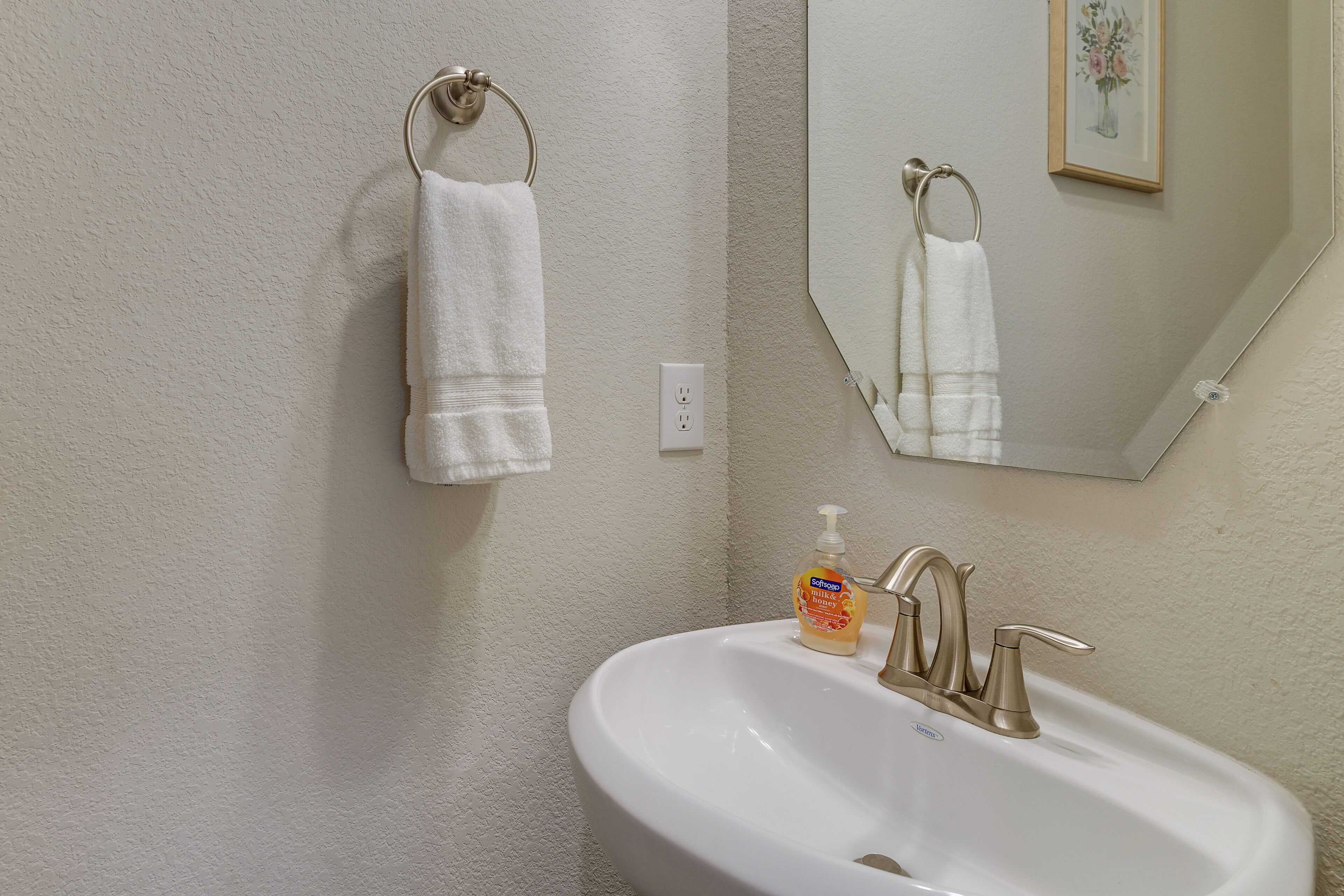 A bathroom with a white sink, a gold faucet, and a white towel hanging on a towel ring.