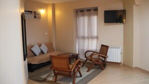 A living room with a sofa, two wooden chairs, a small table, a TV mounted on the wall, and a window with curtains. - hotel balcon de san bartolo (Barreiros)