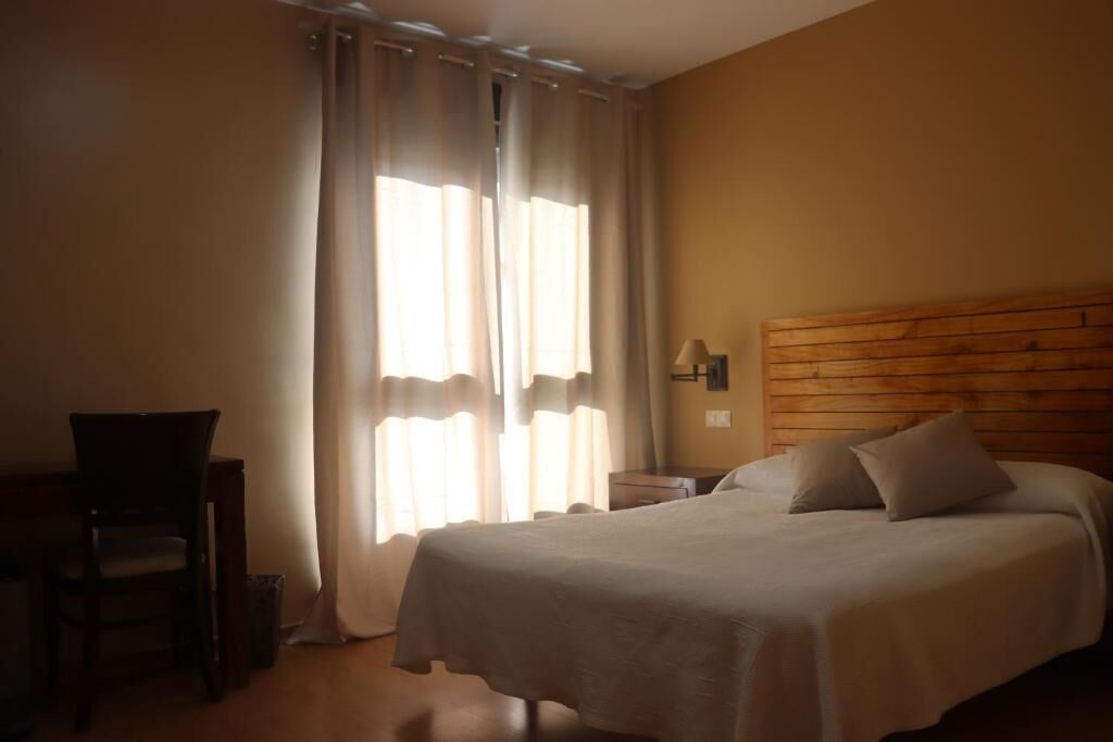 Una habitación de hotel con una cama, una silla, una mesita de noche y una lámpara.