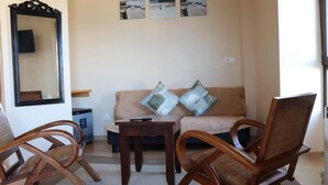 A living room with a beige sofa, two wooden chairs, a small table, and a mirror. There are three framed pictures on the wall above the sofa. - hotel balcon de san bartolo (Barreiros)