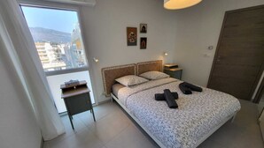 Ein Schlafzimmer mit Bett, Nachttisch, Fenster mit Blick und Tür.
