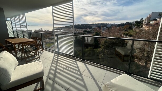 Ein Balkon mit Blick auf eine Stadtlandschaft, einem Holztisch und zwei weißen, gepolsterten Stühlen.