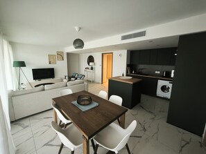 A modern living space with a dining area, a sofa, a TV, a lamp, and a kitchen with a washing machine. - Kosmic 702 by Avecoeur (Roquebrune-Cap-Martin)