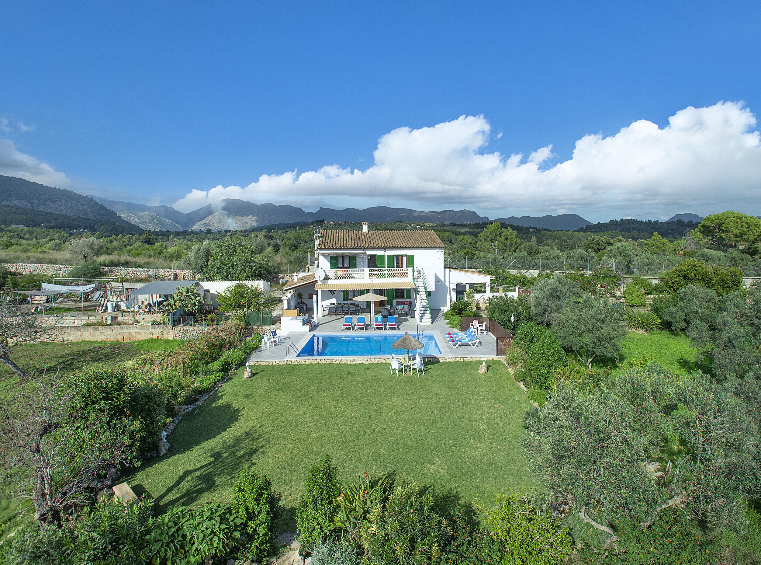 A two-story house with a swimming pool, surrounded by lush greenery and mountains in the background.