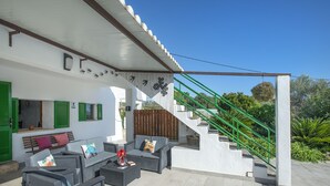 Un espace extérieur aménagé, abrité et doté de mobilier en osier, avec un escalier et de la verdure en arrière-plan.