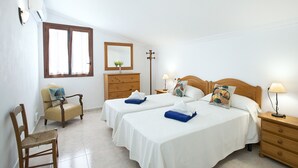 Une chambre d’hôtel avec deux lits, une commode en bois, une chaise, une table de chevet avec une lampe et un miroir au mur.