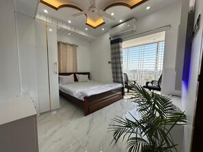 A modern bedroom with a bed, a chair, a large window, and a ceiling fan. - City view hotel and Apartment (Rajshahi)