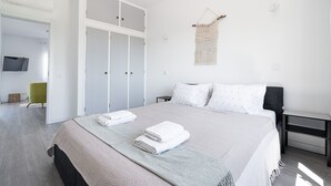 Een slaapkamer met een bed, een kledingkast, een stoel en een televisie op de achtergrond.