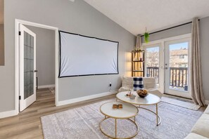 Una sala de estar con una pantalla grande, un sofá, una mesa de centro y vistas al exterior.