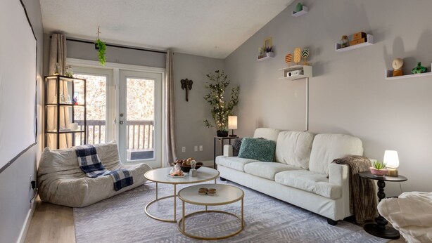 A living room with a white sofa, two round coffee tables, a patterned rug, and a window with curtains.