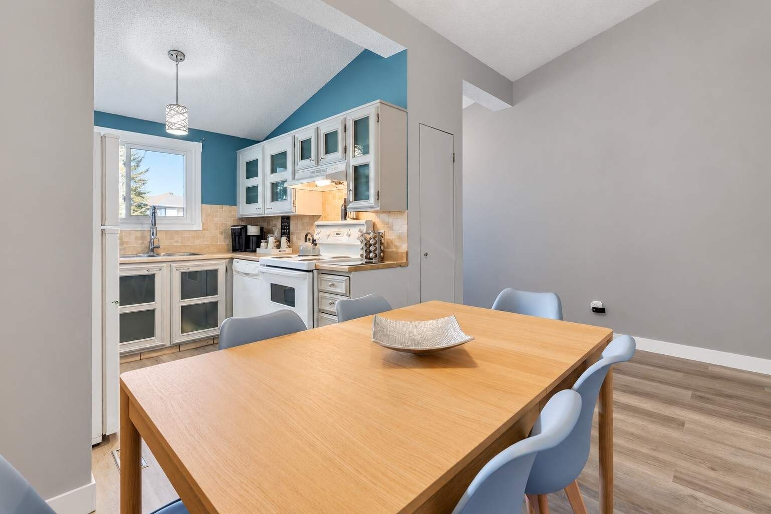 A modern kitchen with white cabinets, a wooden dining table, and blue chairs.
