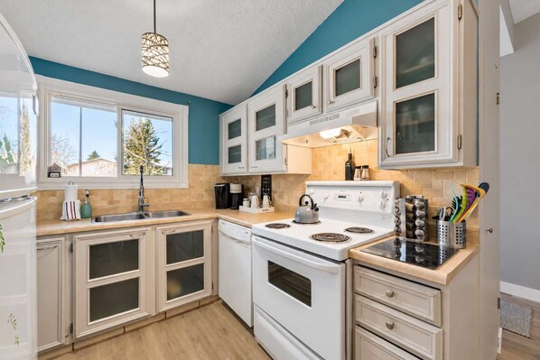 Una cocina con armarios blancos, estufa, fregadero y ventana.