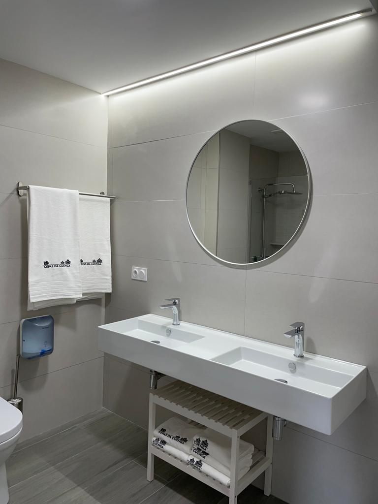A modern bathroom with a dual sink vanity, a round mirror, and a towel rack with two towels.