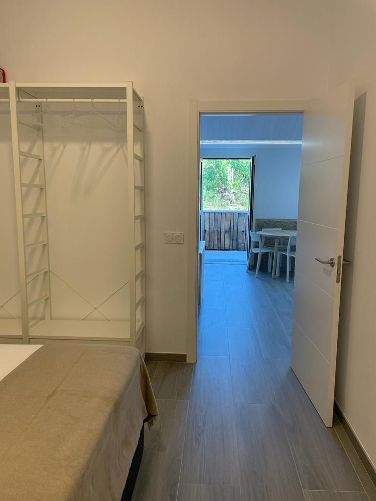 Una habitación con una cama, un armario y una puerta abierta que da a un espacio exterior con una mesa y sillas.
