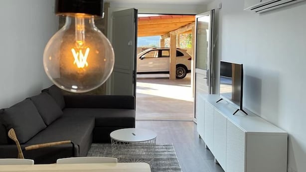 Un salon moderne avec un canapé noir, une table à manger en bois et un luminaire suspendu.