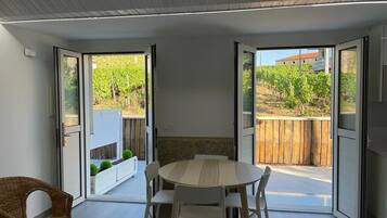 A modern dining area with a round table and chairs, large sliding glass doors leading to a garden with a wooden fence and greenery.