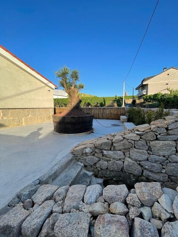 A courtyard with a stone wall, a tree, and a building with a red roof. - CEPAS DA CUENGA (Ribadavia)
