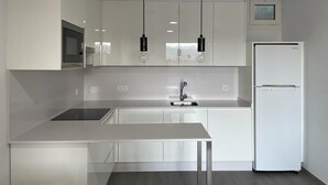 Une cuisine moderne avec des meubles blancs, un évier en acier inoxydable, un plan de travail noir et un réfrigérateur blanc.
