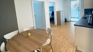Een moderne keuken met een houten tafel en stoelen, een aanrecht met een waterkoker, en uitzicht op het buitenleven door een glazen deur.