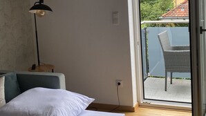 Een slaapkamer met een bed, een bureau, een lamp en een schuifdeur die leidt naar een buitenruimte met een stoel.