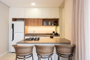 A modern kitchen with white cabinets, a central island, and three wicker chairs. - Apt w/ Barbecue Grill 500m From the Beach Tdf0302 (Itapema)
