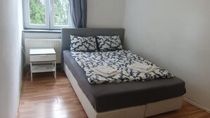 A bedroom with a bed, a radiator, and a window with curtains.