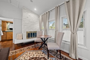 A room with a stone wall, a fireplace, a round table, two chairs, and a patterned rug.