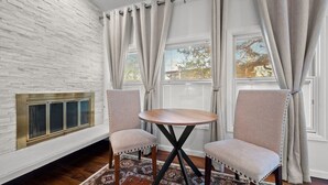 Una habitación con pared de ladrillo blanco, una chimenea, dos sillones tapizados, una mesa redonda y un alfombra con diseño.