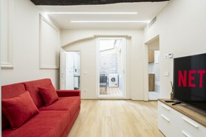 A modern living room with a red sofa, a TV, and a view into a kitchen and laundry area. - [10min Cathedral] Refined Luxury (Firenze)