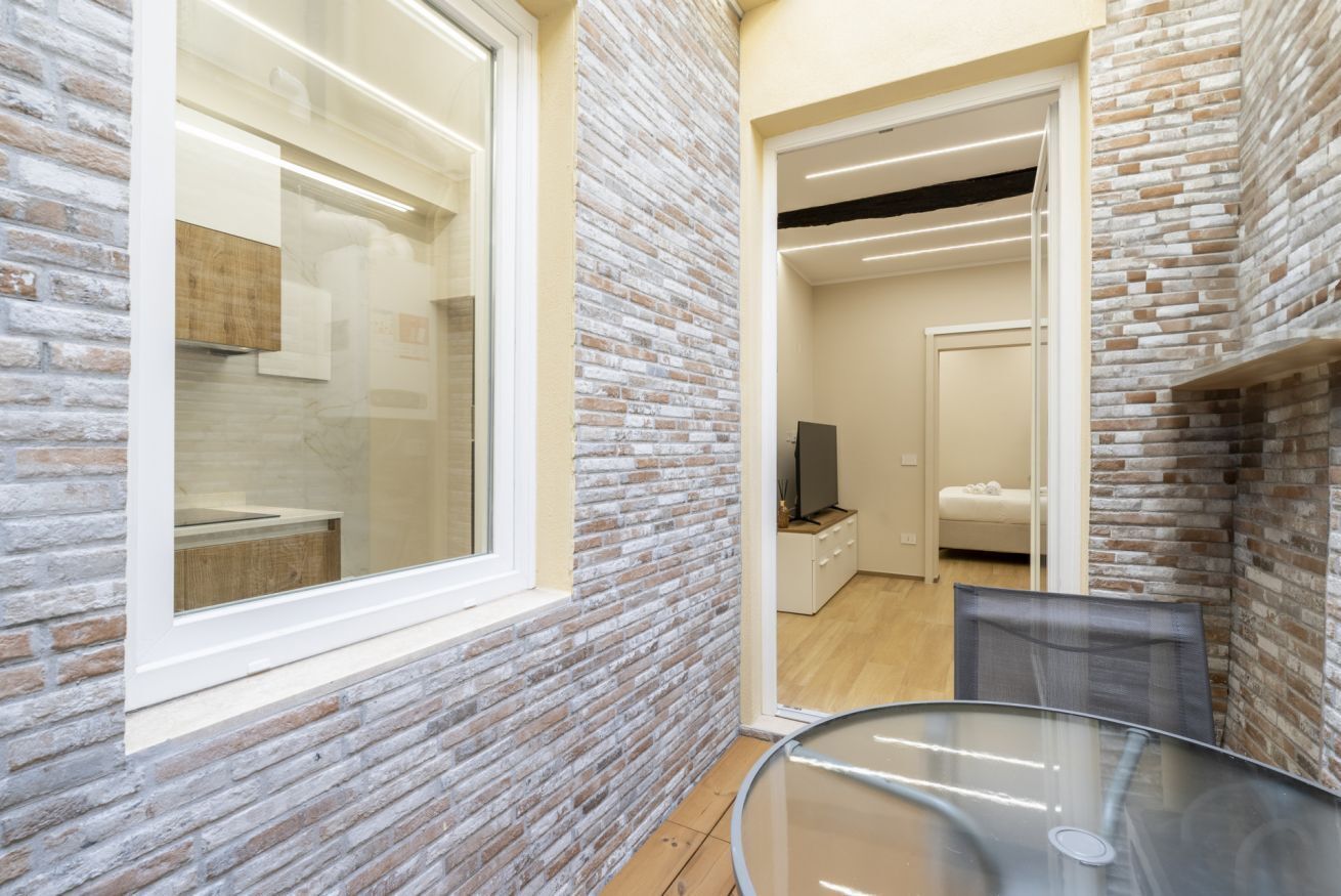 A modern kitchen with a large window, a glass table, and a brick wall.