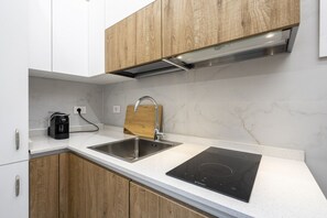 Eine moderne Küche mit Edelstahl-Spüle, Holzschränken, einem eingebauten Ofen und einer Kaffeemaschine.