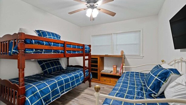 Ein Schlafzimmer mit Etagenbetten, Deckenventilator, Fenster mit Jalousien und Nachttisch mit Lampe.