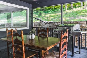 A covered outdoor dining area with a stone wall, a grill, and a view of a wooded area. - A Lakeview Getaway in Guntersville, AL (Guntersville)