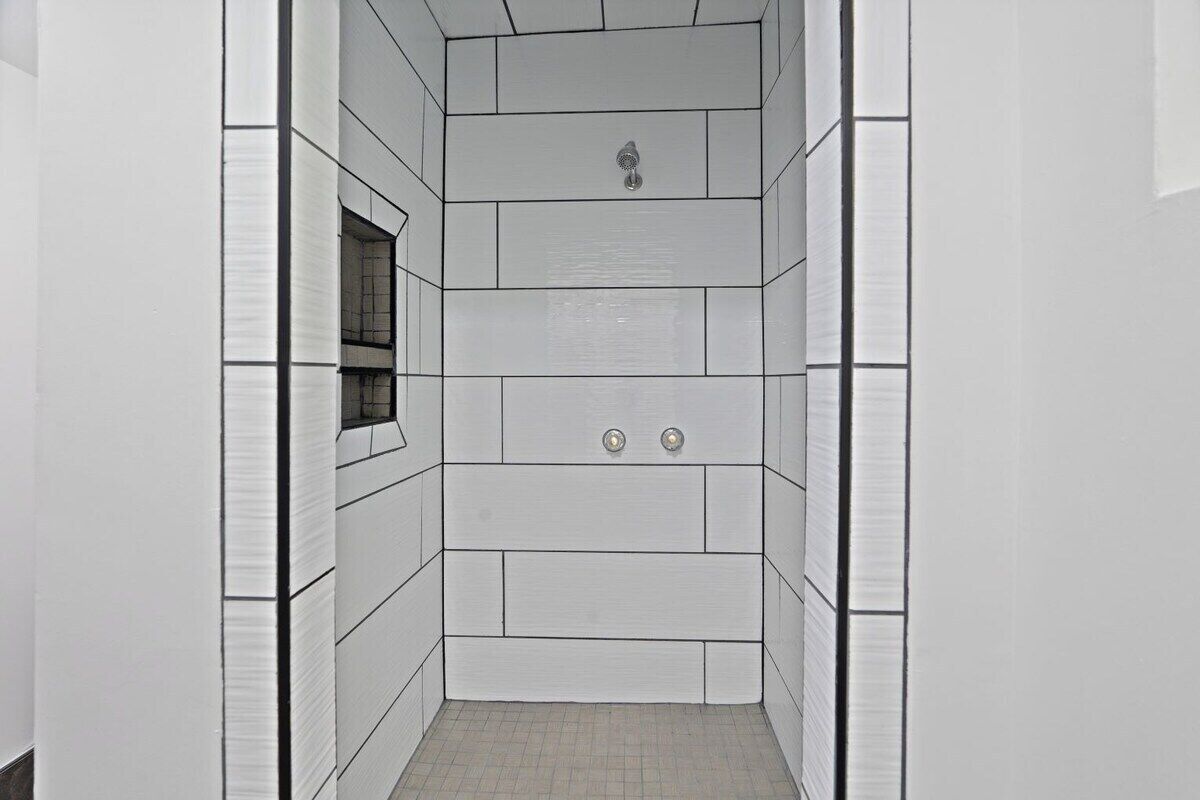 A narrow, tiled shower stall with a window and two wall-mounted controls.