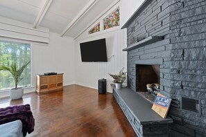 A living room with a stone fireplace, a flat-screen TV mounted on the wall, a wooden cabinet, and a large window. - A Lakeview Getaway in Guntersville, AL (Guntersville)