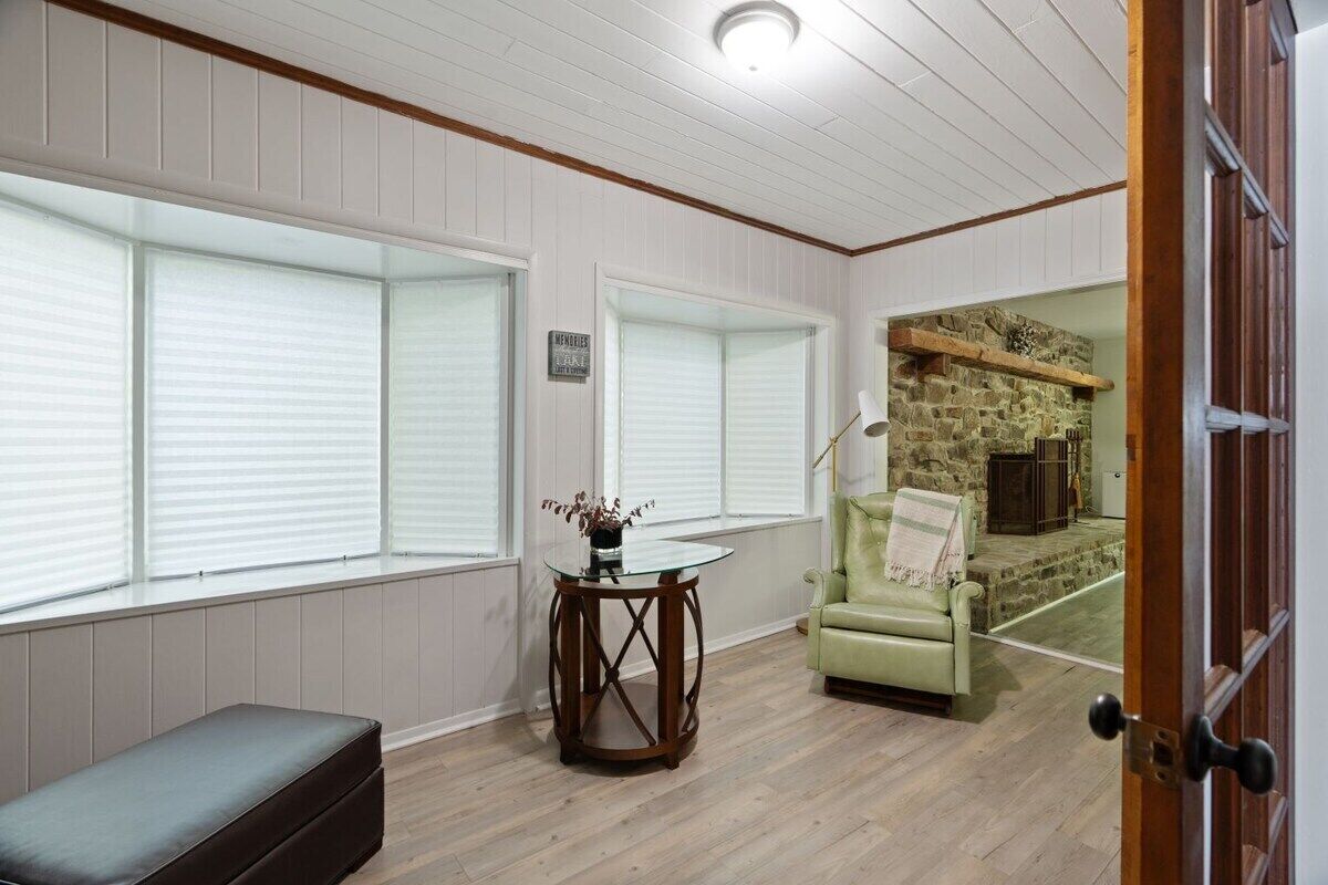 Una habitación con un banco, una mesa, un sillón verde y una chimenea de piedra.