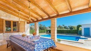 An outdoor dining area with a pool view, stone walls, wooden beams, and a covered patio. - Finca Can Daniel, pool, A/C, Wifi, close to the beach 4 km, quiet location, 3 bedrooms. (Pollenca)